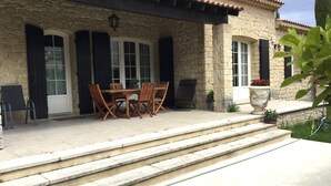 A stone building with a patio, a wooden table with chairs, and steps leading to the entrance.