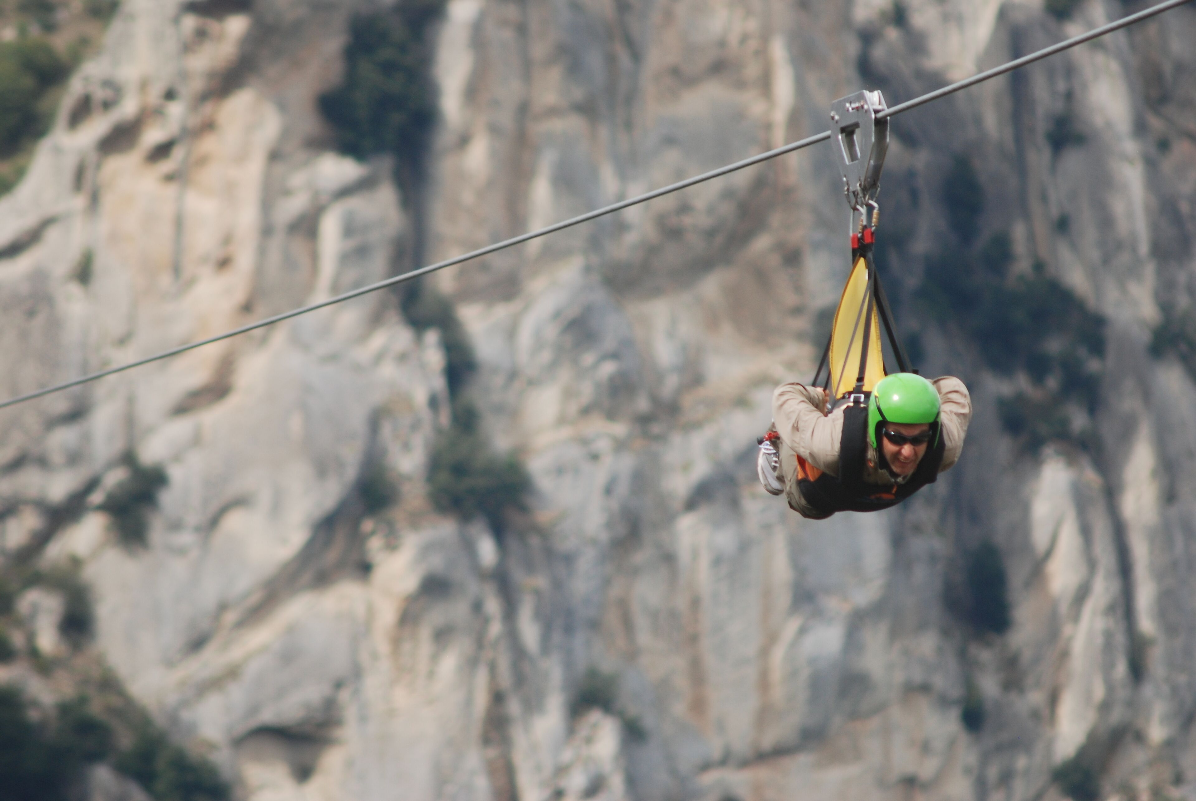 A person suspended in mid-air, attached to a cable, with a mountainous background.