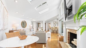 A spacious living area with a white fireplace, a dining area, and a kitchen in the background. - 4 Scaup Court:  A BESTNEST by Beverly Serral (Hilton Head Island)