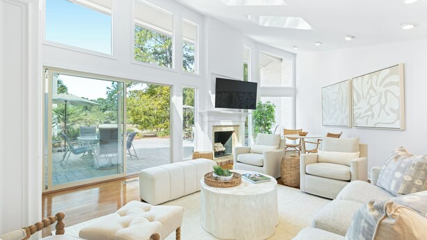 A spacious living room with large windows, a fireplace, and a comfortable seating area. - 4 Scaup Court:  A BESTNEST by Beverly Serral (Hilton Head Island)