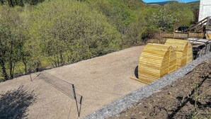 Un paysage rural avec un chemin de terre, des constructions en bois et une colline parsemée d’arbres.