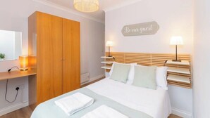 Une chambre à coucher avec un lit, des lampes de chevet, une armoire, une table de chevet avec une lampe et un panneau accroché au mur.