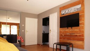 Une pièce comprenant un lit, un téléviseur fixé à un mur en bois, une porte et une petite table.