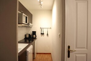 A compact kitchen with a microwave, coffee maker, and hanging utensils.