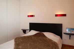 A bedroom with a bed, two bedside tables, and wall-mounted light fixtures.