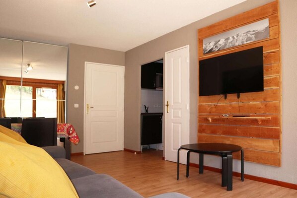 A room with a sofa, a television mounted on a wooden wall, a door, and a small table.