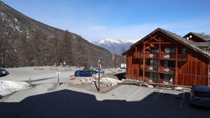 Un chalet en bois doté d’un balcon, d’un espace de stationnement et offrant une vue sur des montagnes enneigées.