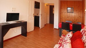 Un salon doté d’un plancher en bois, d’un bureau noir avec un ordinateur, d’un canapé rouge et blanc à motifs et d’un mur en bois orné d’un tableau encadré.