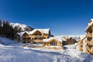 A snow-covered lodge with multiple wooden buildings, a ski slope, and mountains in the background. - Ski-in/ski-out & foot of the slopes, 1st floor, view valley, swimming pool, sauna, hammam, balcony (Les Orres)
