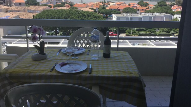 A balcony with a table set for two, overlooking a cityscape with buildings and a distant mountain range. - PLEASANT STUDIO CABIN PARKING SEA AT 80M (Canet-en-Roussillon)