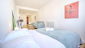 A hotel room with a bed, a blue blanket, a poster on the wall, and a view into the hallway. - 2 person design cozy studio heart of Cannes; Feel at home - Olam Properties (Cannes)