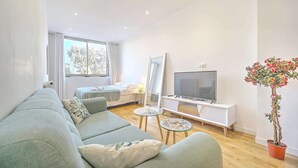A modern living room with a sofa, a TV, a small table, and a potted plant. - 2 person design cozy studio heart of Cannes; Feel at home - Olam Properties (Cannes)