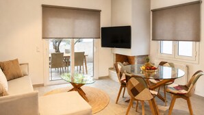 Een moderne woonkamer met een glazen eettafel, comfortabele zitmogelijkheden, een flatscreen televisie en grote ramen met zonwering.