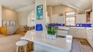 A modern kitchen with a large island, white cabinetry, and a blue backsplash. - Duck Tales | 2400 ft from the beach | Private Pool, Hot Tub | Duck (Duck)