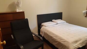 Une chambre à coucher comprenant un lit, une chaise, une commode et un ventilateur fixé au mur.