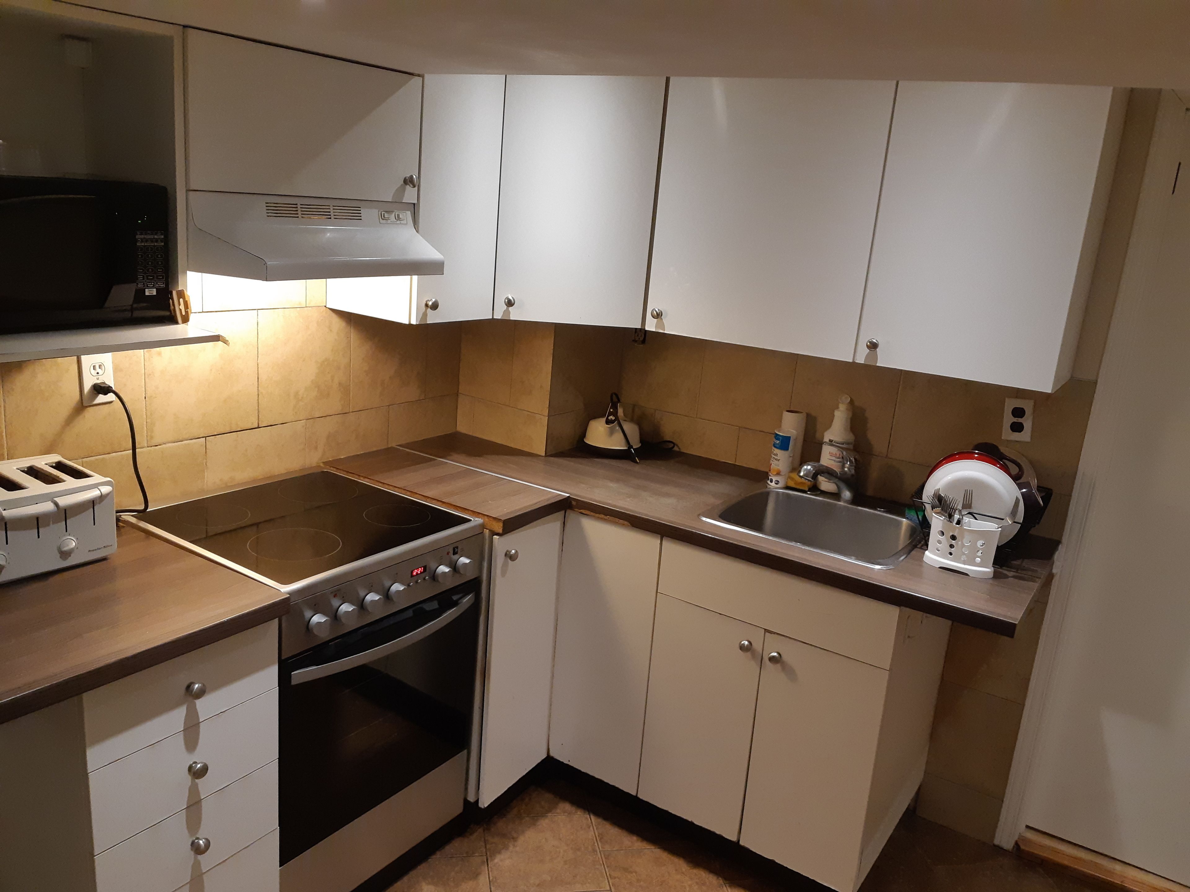 Een kleine keuken met een kookplaat, oven, magnetron en spoelbak.