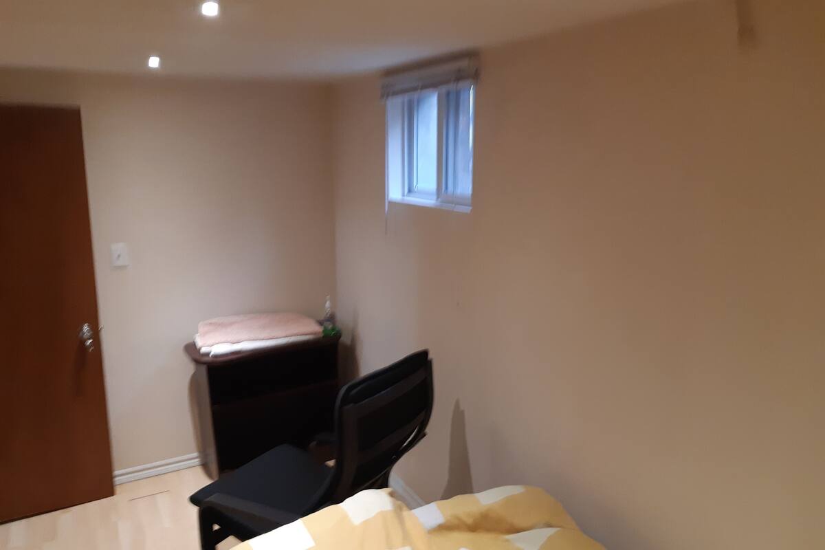 A bedroom with a bed, a chair, a small window, and a door.