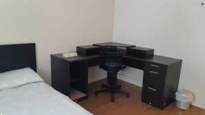 Un dormitorio con cama, escritorio, silla y un cubo de basura.
