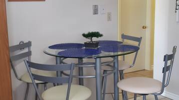 A dining area with a round glass table surrounded by four chairs, a small potted plant, and a painting on the wall.
