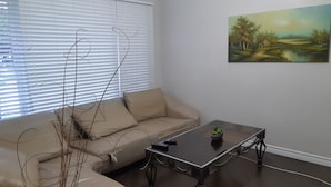 Una sala de estar con un sofá seccional color beige, una mesa de centro de vidrio y un cuadro en la pared.