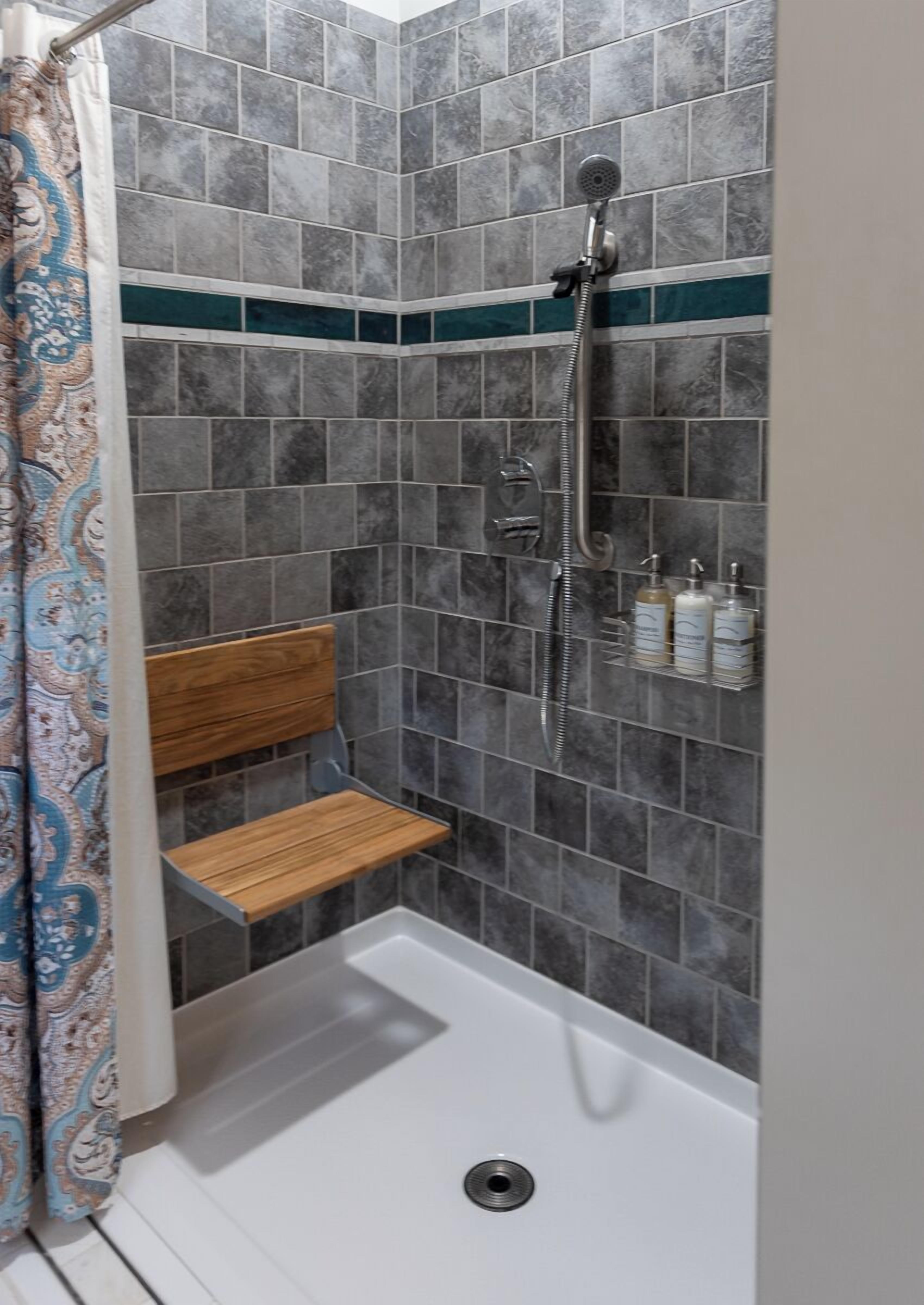 A shower area with grey tiles, a wooden shelf, and a showerhead.