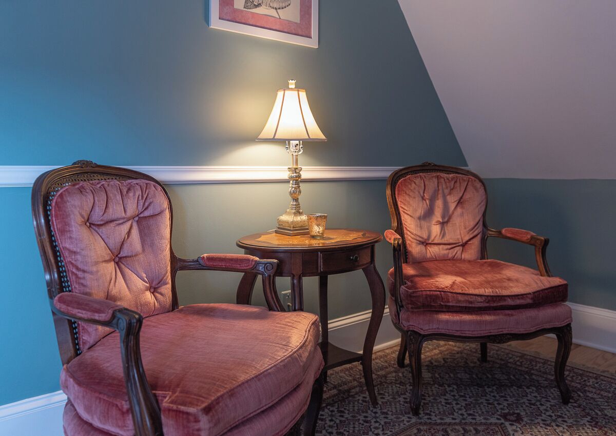 A room with two upholstered chairs, a small round table with a lamp, and a patterned rug.