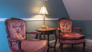 A room with two upholstered chairs, a small round table with a lamp, and a patterned rug.