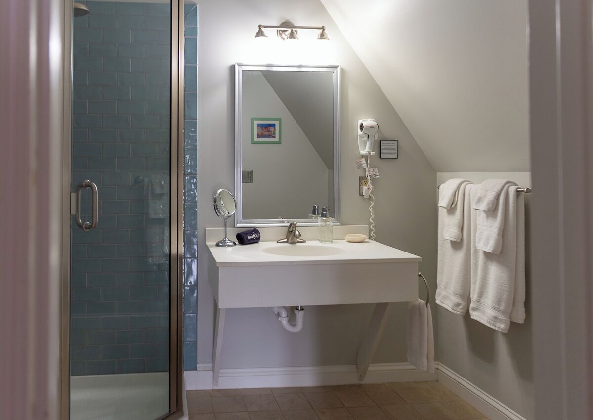 Un baño con cabina de ducha de vidrio, un lavabo blanco con espejo y un perchero para toallas.