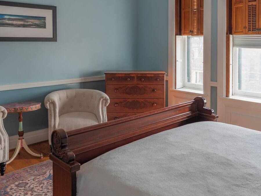 Ein Schlafzimmer mit einem hölzernen Bett, einem kleinen runden Tisch, einem weißen Sessel und einer Kommode.