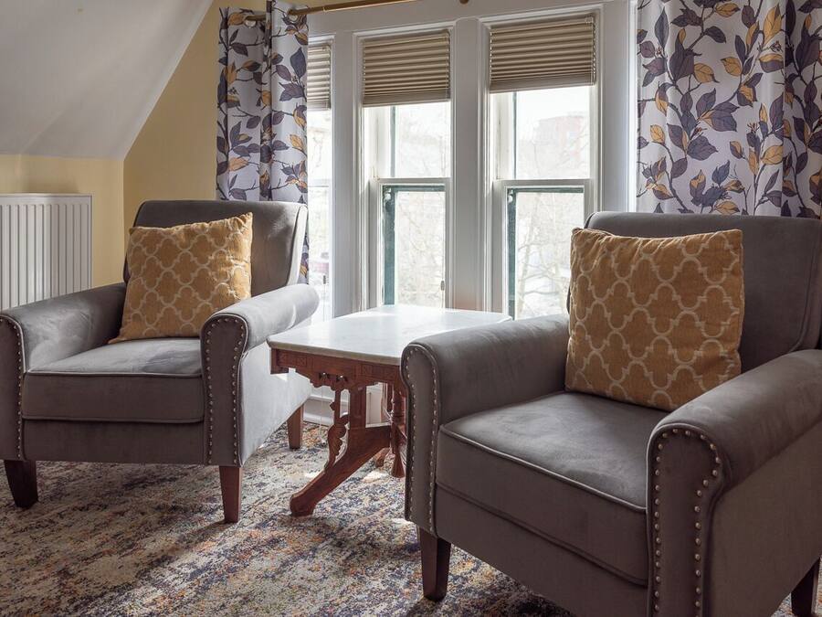 A cozy living room with two armchairs, a wooden coffee table, and patterned curtains.