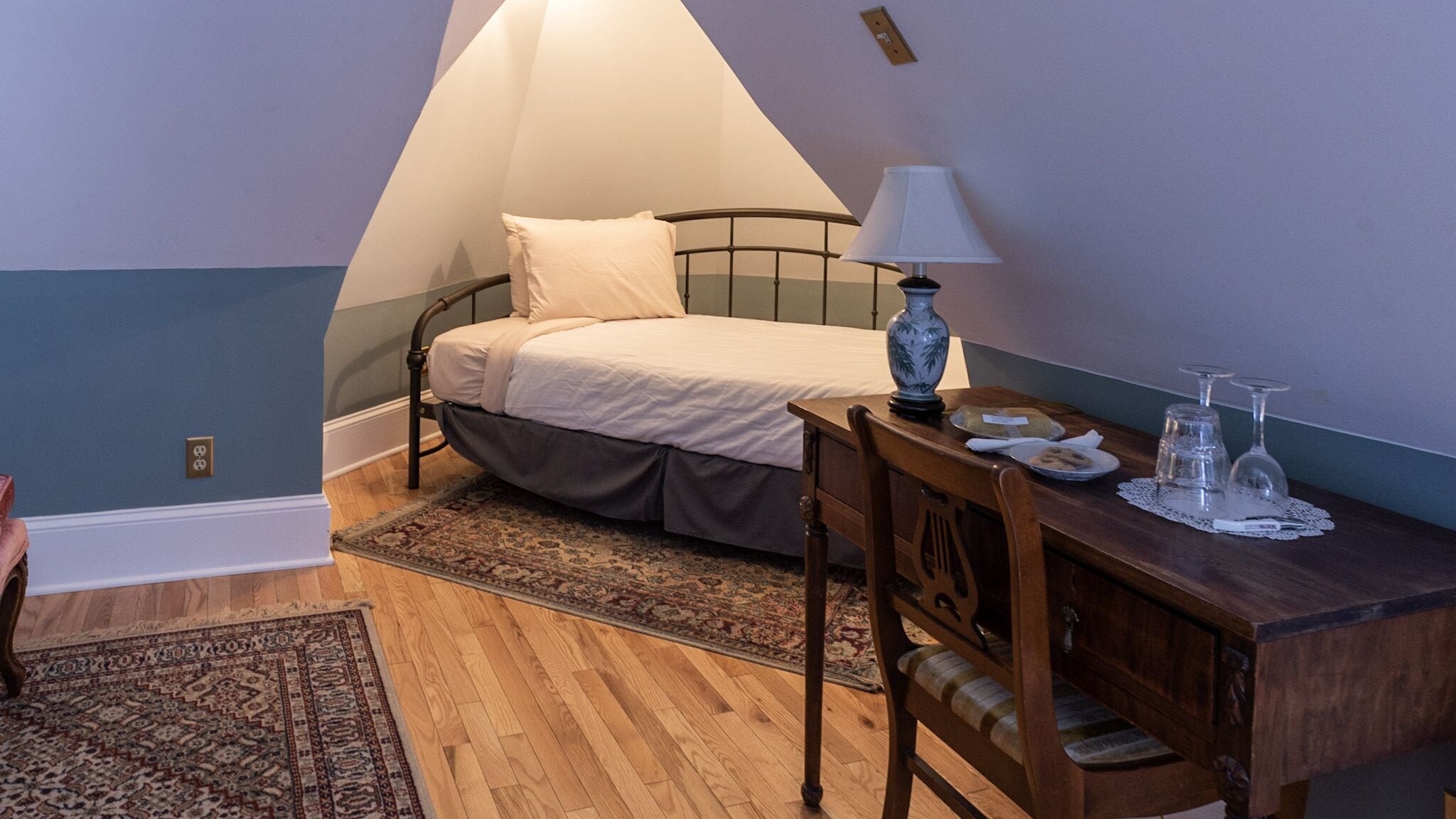 A bedroom with a bed, a desk with a lamp, and a chair.