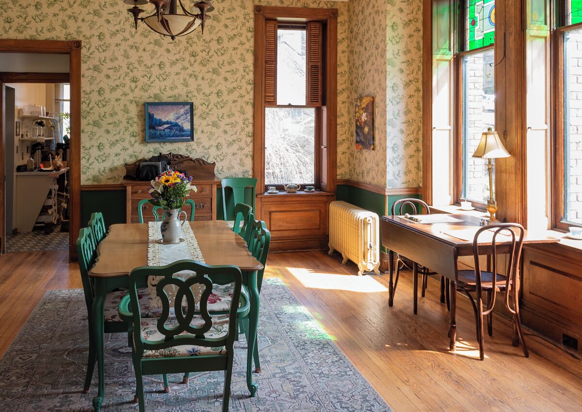 Une salle à manger avec une table en bois, des chaises vertes, un radiateur et une fenêtre avec des volets.