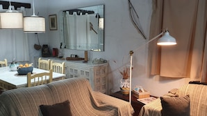 Ein gemütliches Wohnzimmer mit Essbereich, inklusive Tisch mit Stühlen, einer Couch, einer Lampe und einem Spiegel an der Wand.