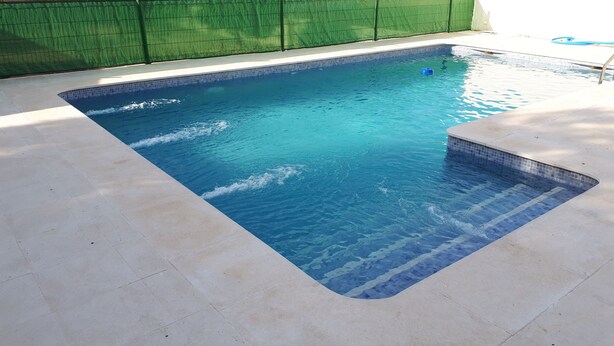 Ein rechteckiger Swimmingpool mit klarem, blauem Wasser, umgeben von einer gefliesten Liegefläche.