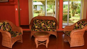A room with three wicker chairs and a small table, a red wall, and a view of a garden through glass doors. - Hotel Arbol Dorado (Florencia)