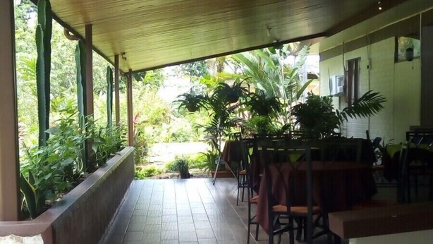 A covered outdoor area with tiled flooring, wooden pillars, and a row of chairs and tables. - Hotel Arbol Dorado (Florencia)