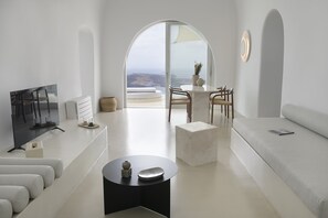 A modern living room with a flat-screen TV, a round coffee table, a sofa, and a dining area with chairs and a table.