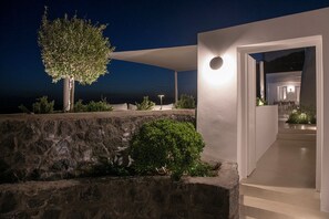 A modern house with a stone retaining wall, a tree, and a well-lit entrance.