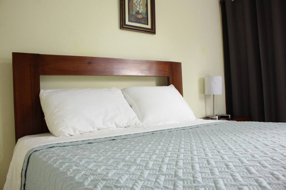 Una cama bien hecha con tablero de madera, almohadas blancas y colcha acolchada.