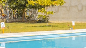 Una piscina con césped y árboles al fondo.