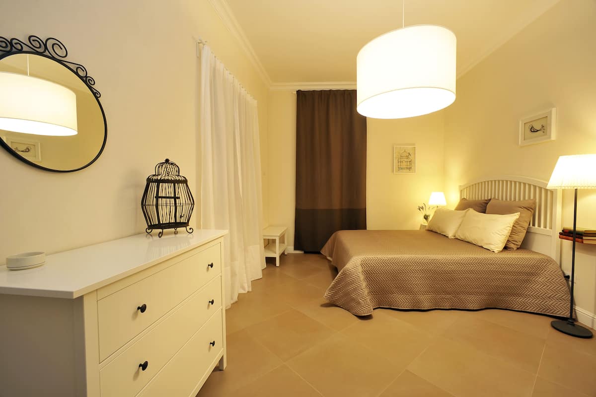 Une chambre à coucher avec un lit, des lampes de chevet, une commode, un miroir et une fenêtre avec des rideaux.