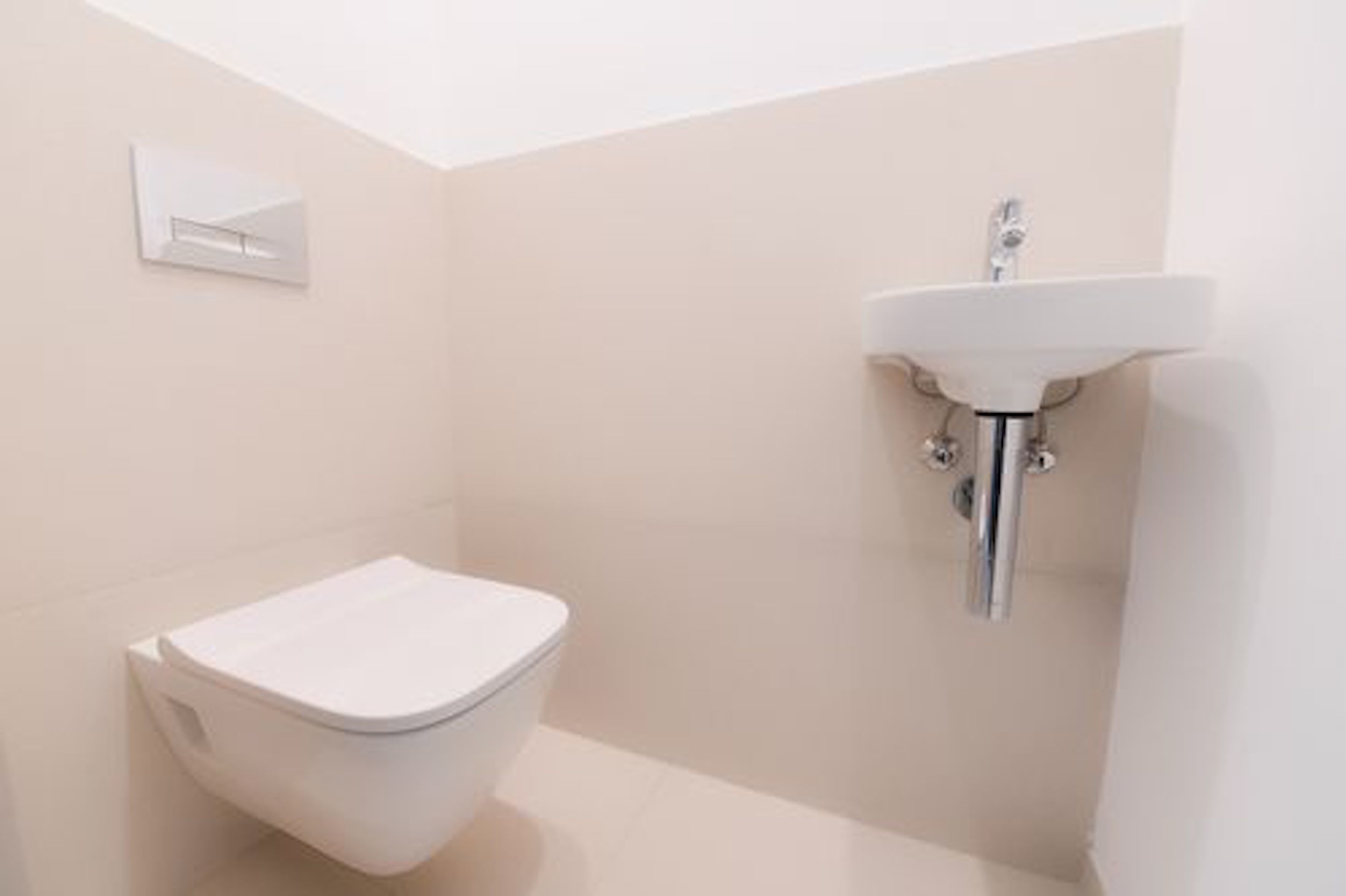 A modern bathroom with a toilet, a wall-mounted sink, and a light switch.