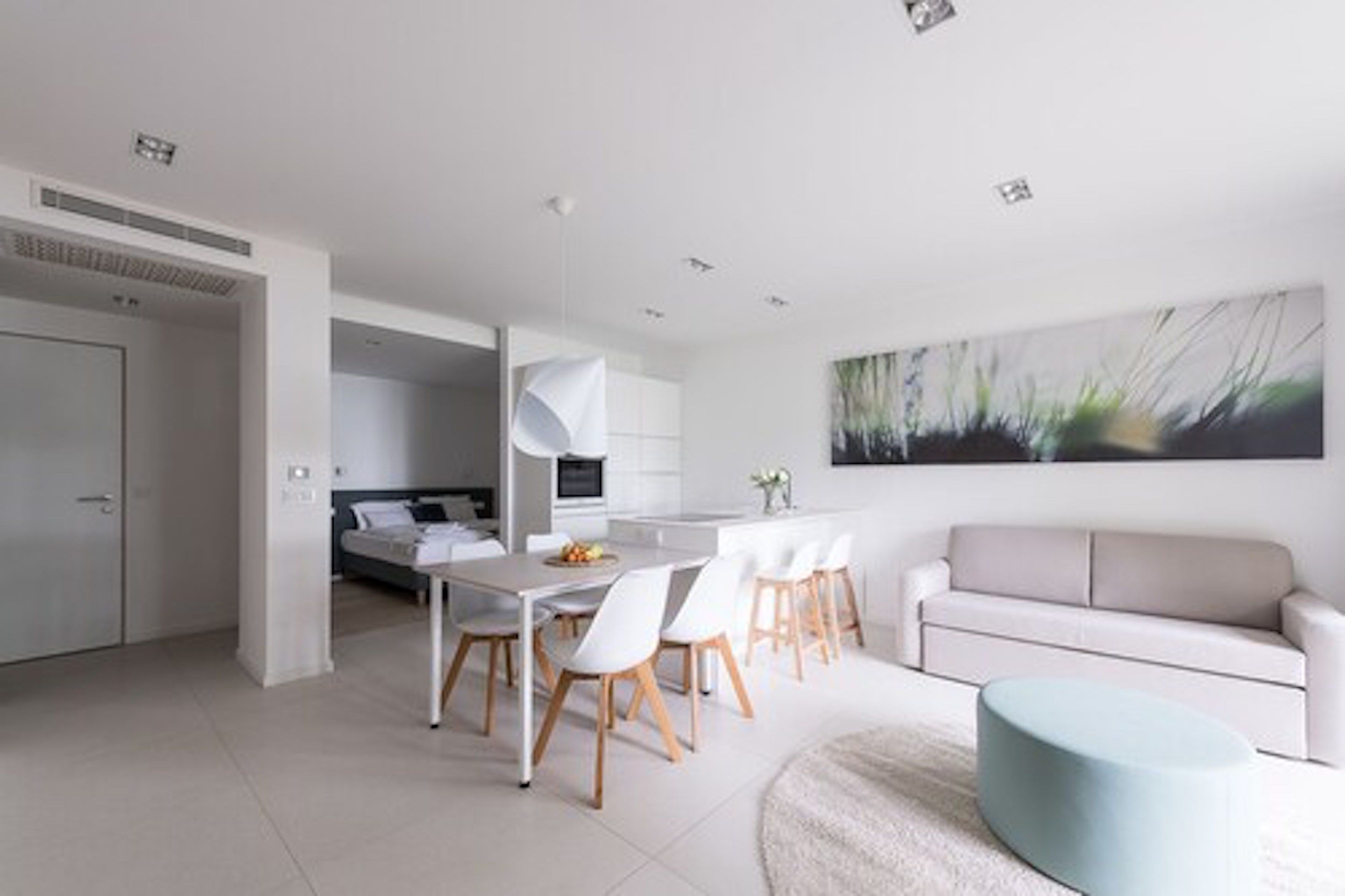 A modern kitchen with white cabinetry, a dining area with a white table and chairs, and a light blue ottoman.