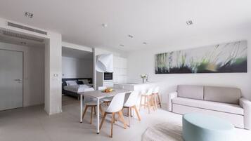 A modern kitchen with white cabinetry, a dining area with a white table and chairs, and a light blue ottoman.