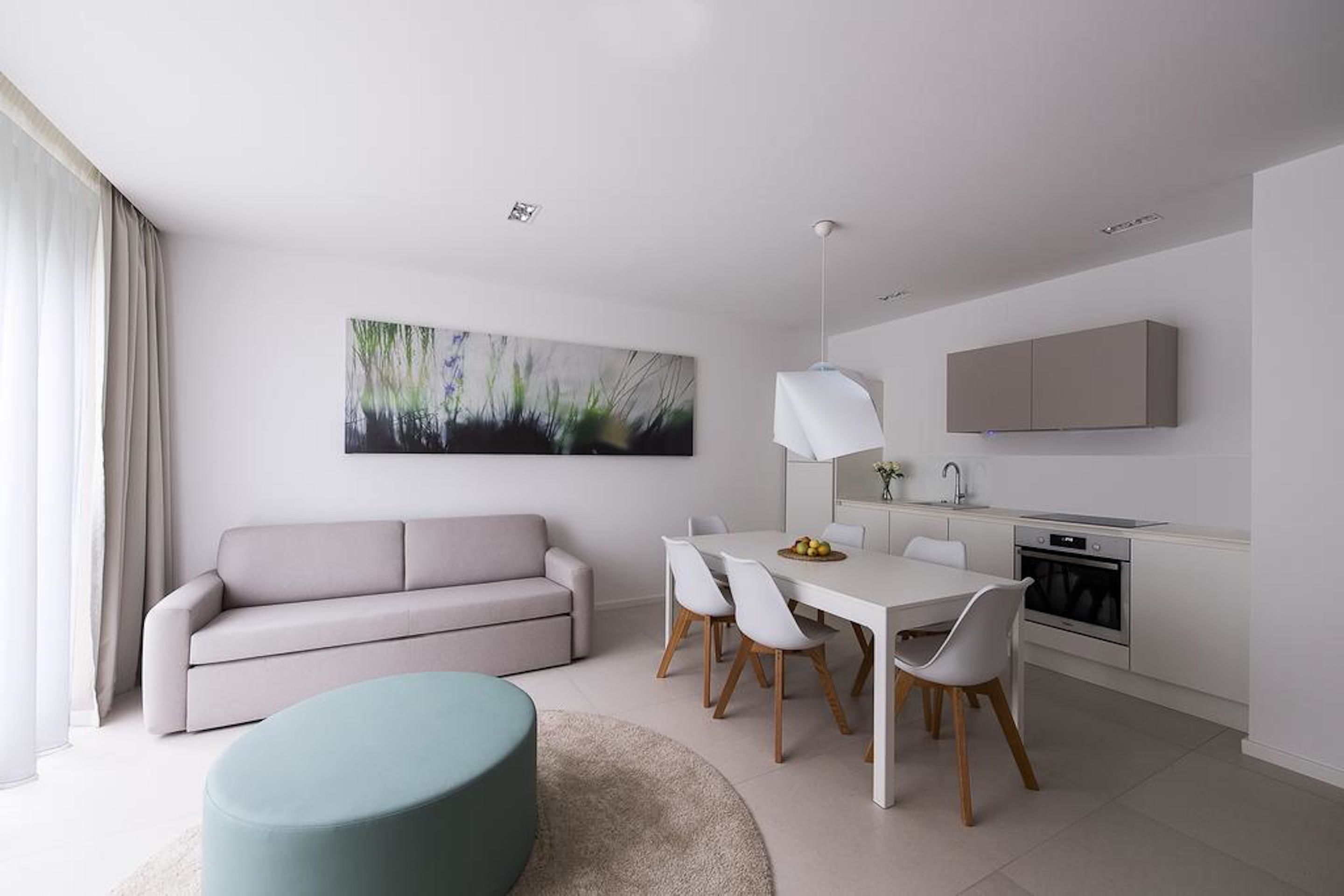 A modern living room with a sofa, dining table, chairs, and a kitchen area with cabinets and appliances.