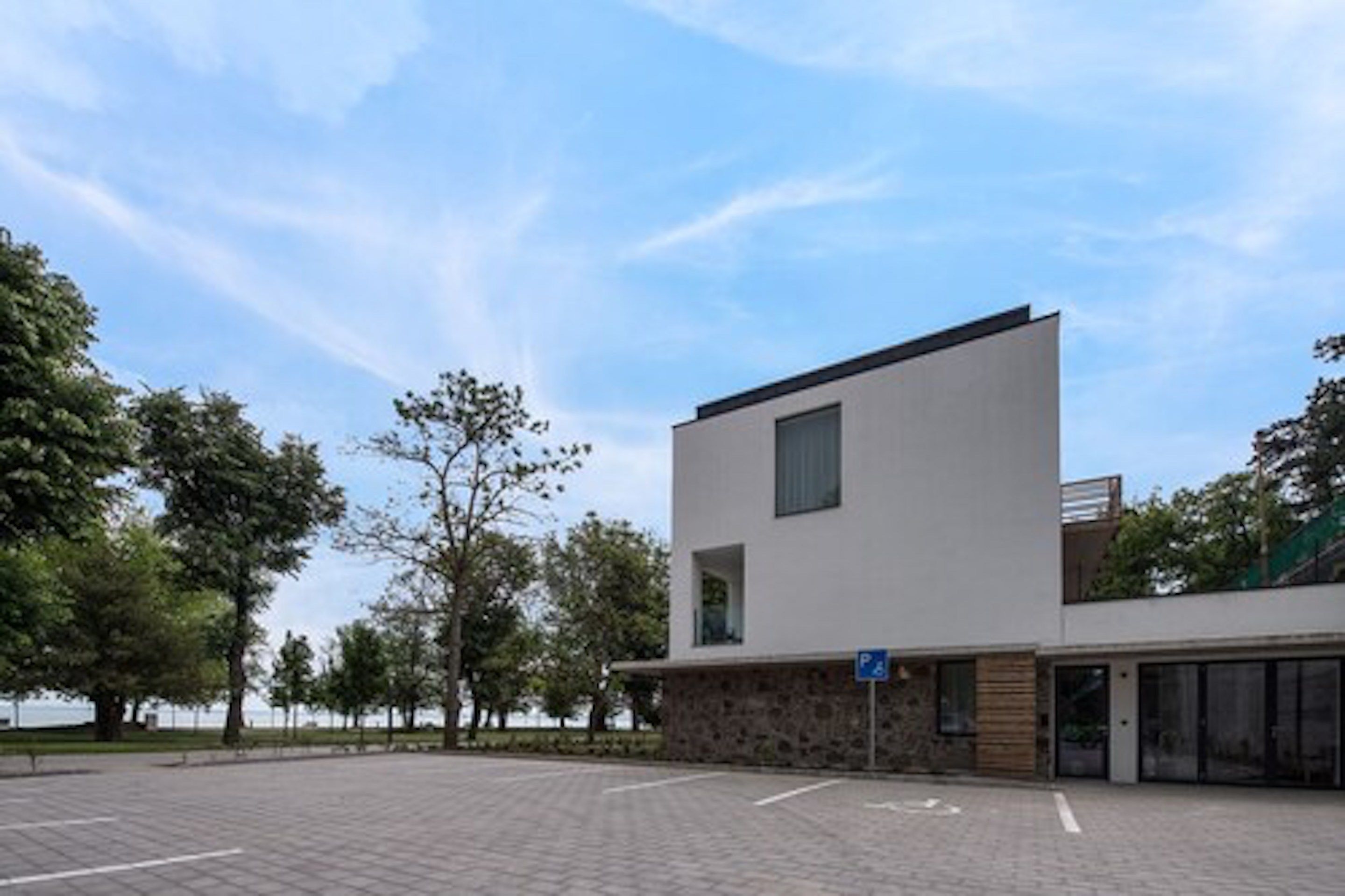 Een modern gebouw met een plat dak en een stenen basis, met een blauw parkeersbord.
