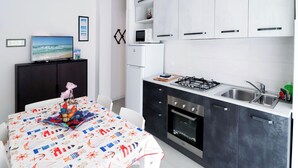 A modern kitchen with white cabinets, a gas stove, and a microwave. There is a dining table with a colorful tablecloth and a decorative centerpiece.