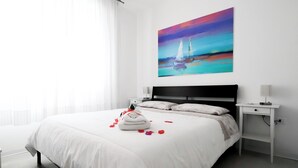 A modern bedroom with a large bed, a nightstand, and a wall-mounted painting.