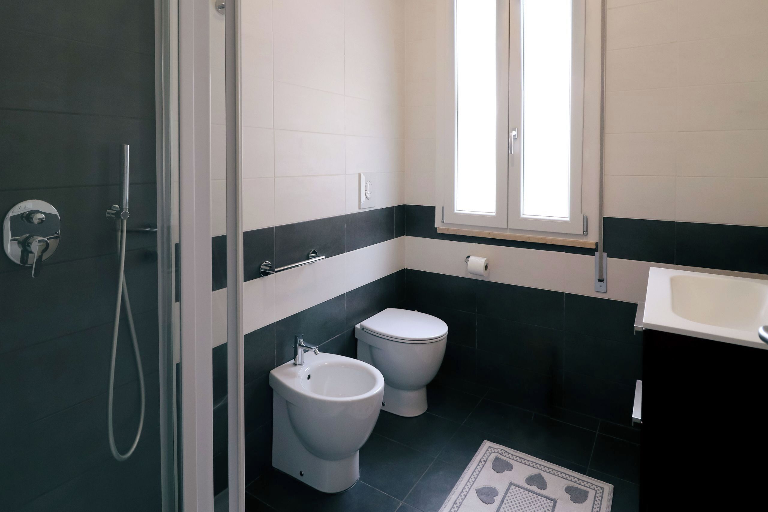 A bathroom with a shower, two toilets, a bidet, and a sink.