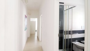 A hallway leading to a bathroom with a glass shower enclosure and a sink.